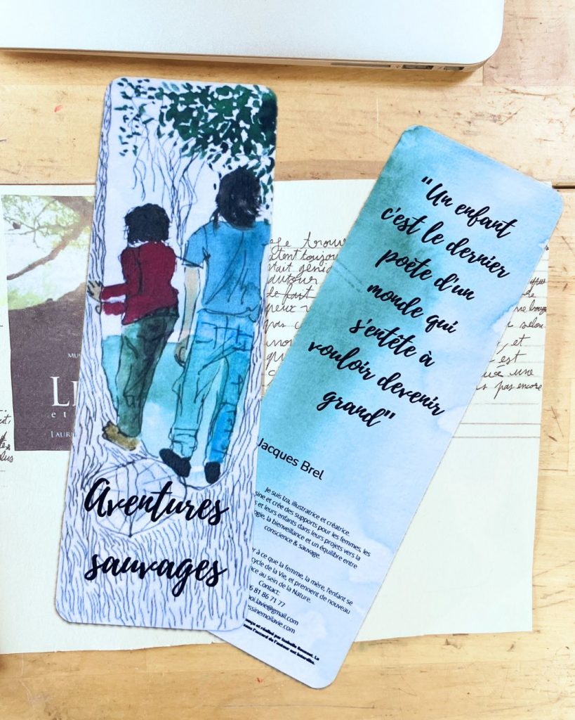 Le marque-pages "Aventures sauvages, vue du recto et du verso posées côte à côte. Le fond est travail d'un enfant sur papier, et un ordinateur, posés sur une table en bois.