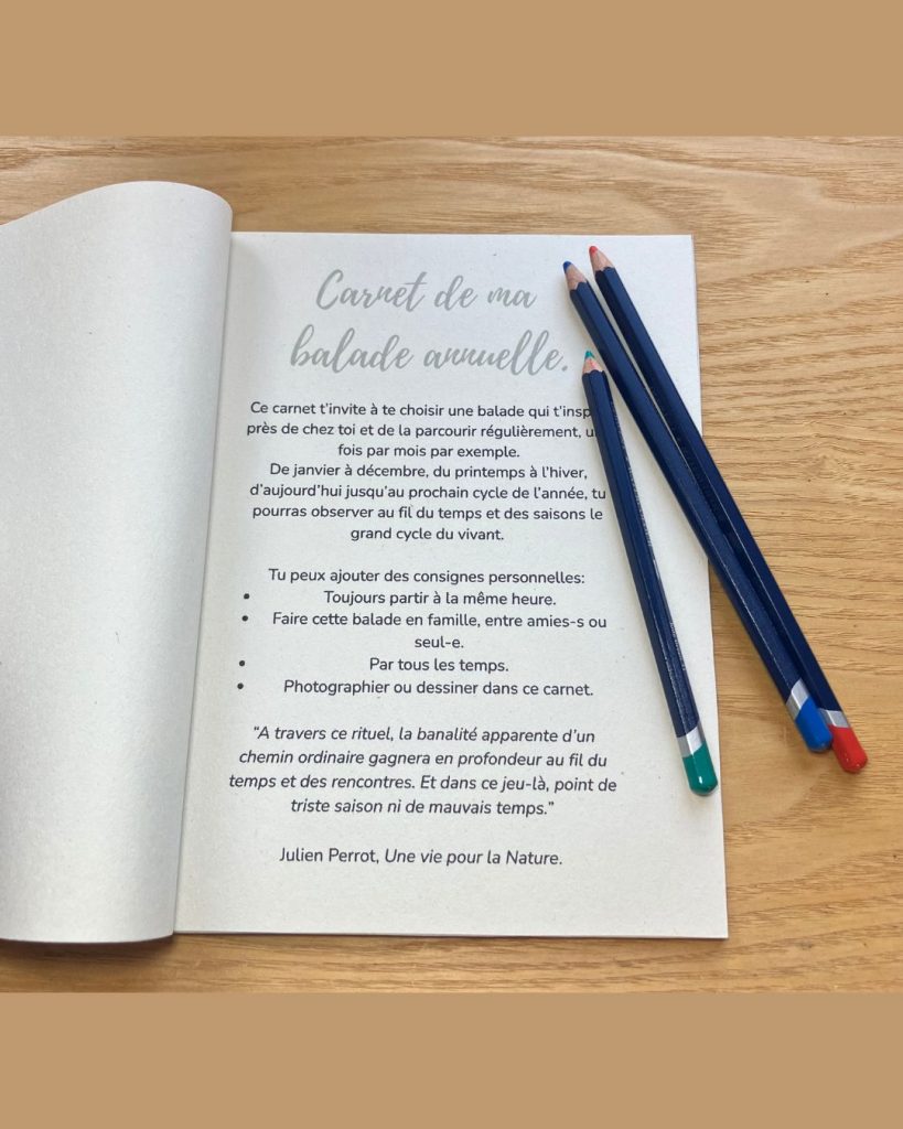 Carnet "Aventures sauvages", ouvert à la première page, un texte descriptif de l'utilité de ce carnet. Des crayons de couleurs invitent à prendre ses crayons pour le remplir. Il est posé sur un support en bois.
